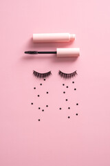 Flat lay composition with mascara, false eyelashes with tears made of confetti on pink background.