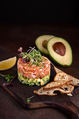 delicious avocado and salted salmon tartare, served with young herbs, dark background, selective...