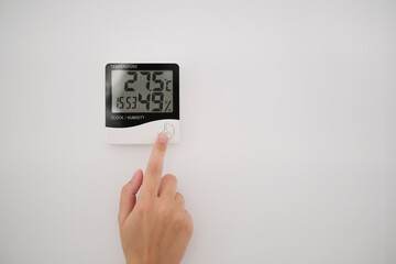the girl adjusts the psychrometer at home. device for measuring humidity and temperature on a white wall close-up.