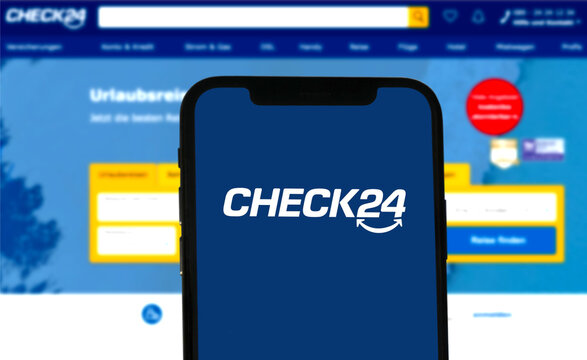 Smartphone zeigt Check 24 Logo an, im Hintergrund die Website des Vergleichsportal f&uuml;r Versicherungen, Finanzen, Energie, Telekommunikation, Reisen und Shopping