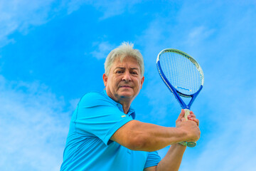 Senior man playing tennis on sunny day.