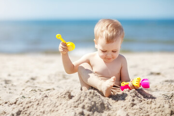 A boy plays on the beach in the sand. The child is digging a hole