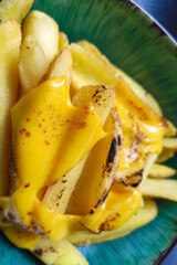 Delicious French fries with cheese in a green plate in a restaurant.