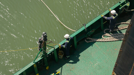 Two seafarers pulling and holding the mooring line during mooring of cargo ship