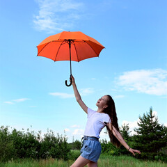 beautiful young girl white T-shirt and denim shorts holds orange umbrella high above her head. Walk...
