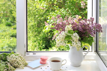 Home interior with decor elements, beautiful spring lilac branches in a vase on a sunny window, abstract flower arrangement, still life with place for text, floral birthday card, wedding,