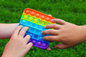 Child's hands are played square multicolored bubble toy antistress sensory pop it.