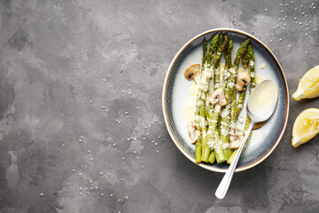 Baked asparagus and mushrooms with sauce in a plate on a gray background, place for text. Top view.