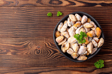 Frozen seafood with green parsley in a black dish on wooden background, top view with empty space.