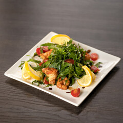 Fresh salad of arugula, tomatoes, lemon and fried shrimp on square plate. Object on wooden blurred background. Soft focus. Copy space.