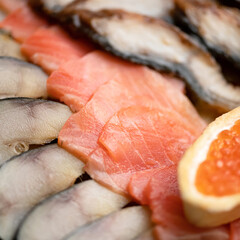 Close-up of Seafood plate. Slices of red salmon fish, pieces of mackerel and sandwich with red caviar in foreground. Soft focus.