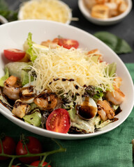 Caesar salad. Bowl of delicious snack or appetizer of chopped vegetables, grated cheese and seafood. Close-up shot. Vertical format. Soft focus.