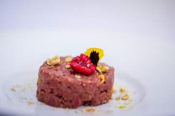 raw meat tartare macro with raspberry and nuts on white plate