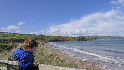 Red headed boy with blue jacket leaning on a wooden fence on sandy beach