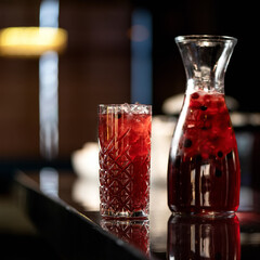 Glassware with red berries and mint lemonade drink on backlit blurred background. Healthy fresh juice or soft drink. Bright colors of nature. Side view. Soft focus.