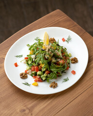 Platter with raw cucumbers, tomatoes, arugula and walnuts on wooden table. Vitamin mixed salad of fresh herbs and vegetables. Vegetarian vegan food. Healthy eating. Copy space.