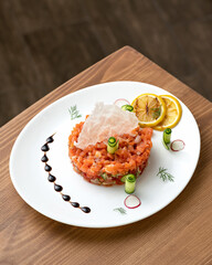 Appetizer of red sturgeon fish and vegetables. Platter with salmon pieces, lemon slices and cucumber rolls on on wooden table. Top side view. Copy space. Vertical format.