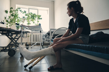 A woman with a broken leg sits on a hospital couch and looks out the window. Leg injury. Loss of...