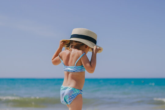 little beautiful girl walks on the sea on the beach in a mermaid swimsuit and a straw hat with a ribbon