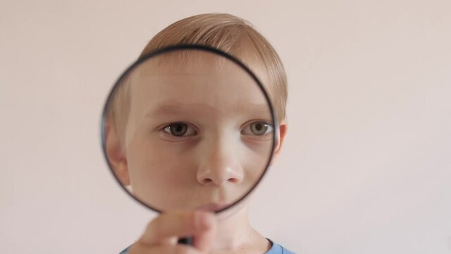 Closeup portrait on cute little boy playing applying magnifying glass zoom face lips nose eyes
