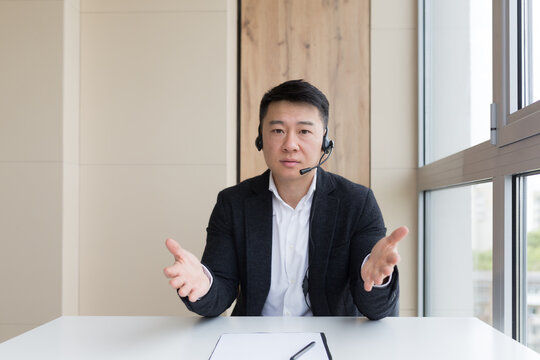 young asian male businessman talking online on video call, conference or meeting looking at camera. Webcam view. Asia Man in business suit indoors. Office negotiations distance Consultation or advice