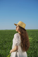 Obraz premium girl in a straw hat and a sundress against the background of a green field and a clear blue sky