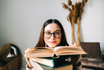 Portrait of young caucasian woman college student in eyeglasses with stack of books, looking at camera.