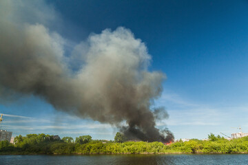 A huge column of black smoke rises from a fire near the river