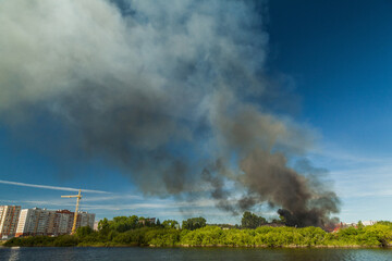 Fototapeta na wymiar A huge column of black smoke rises from a fire near the river
