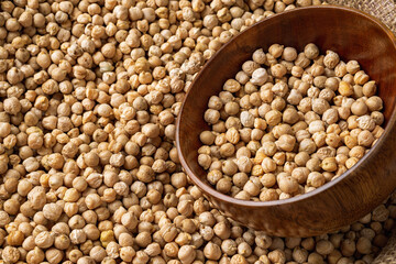 Raw chickpeas in a wooden bowl in a bag of chickpea beans. Legume dietary fibers and vegetable protein for healthy eating. Dry organic chickpeas for cooking hummus. Copy space.