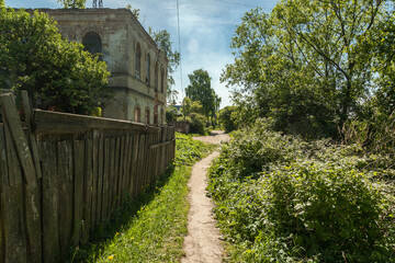 Small overgrown path past an abandoned house among green trees