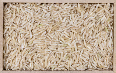 top view of brown integrel rice (Oryza sativa) seeds in a rectangular wooden box.
