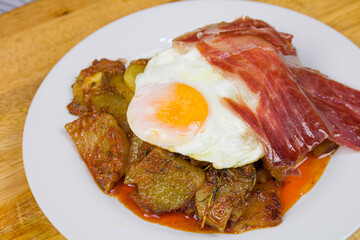 Spanish typical tapas: eggs with Serrano ham recipe. Broken eggs, serrano ham slices and potatoes...