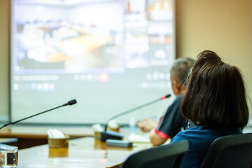 Selective focus to business woman with blurry business man speaking to desktop conference microphones and projector  in a meeting room. Background of business meeting and presentation.