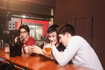 A man showing an image to his friends from his smart phone, while drinking beer at the bar.