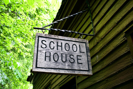 Wooden school house sign hanging outside a log cabin 
