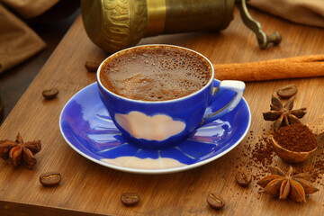 Coffee beans and ground coffee in wooden spoons on brown background. With coffee pot, blue coffee cup and coffee grinder. 