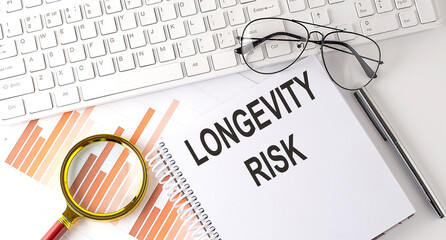 LONGEVITY RISK text written on a notebook with keyboard, chart,and glasses