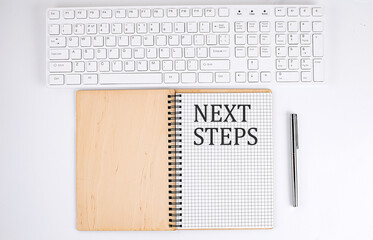 NEXT STEPS text on the notebook with keyboard on white background