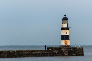 Obraz premium Man fishing by the lighthouse in Seaham