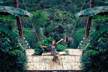 Beautiful woman sitting on swing open arms smiling on the top of the green valley over mountain...