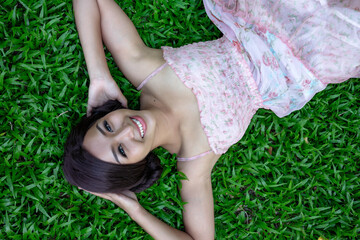 Young asian woman holding hair smiling lay on green grass background