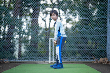 Active boy playing cricket. Young Indian child holding cricket bat in front of wickets in the nets at park