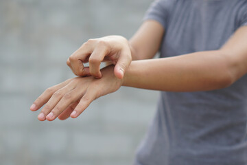 Woman scratching arm from itching on light gray background. Cause of itchy skin include insect...
