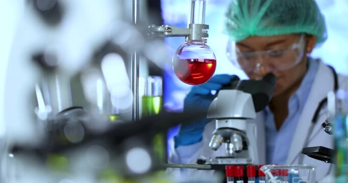 Pan shot of a working female asian scientist in the laboratory with multiple lab equipment and microscope. Healthcare technology and pharmaceutical research and development concept.