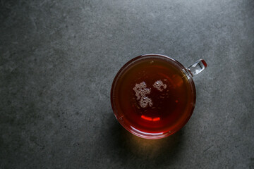 A cup of hot, black tea in a glass cup on a gray ceramic countertop.