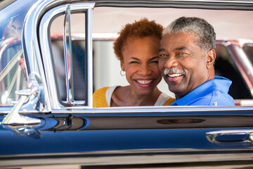 Older couple sitting in a classic car looking to camera smiling