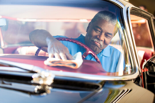 Older man sitting in drivers seat of 1960 Oldsmobile Super 88 Holiday Sport Sedan, wiping down dash with dust cloth 