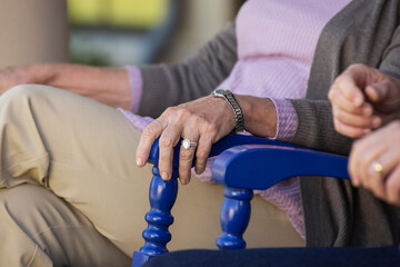 Older couple sitting in rocking chairs, detail on woman hand with ring resting on a chair