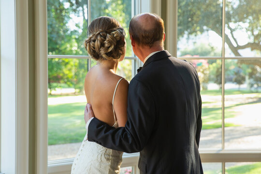 Bride and her father looking out window of home 